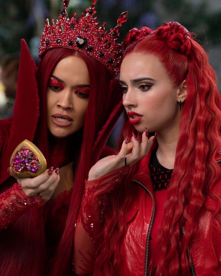 two women with red hair and makeup are dressed in costumes, one is holding a cookie