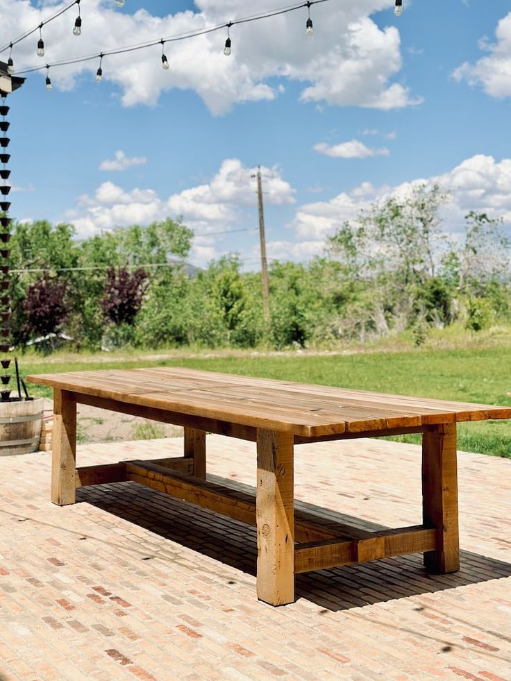 a wooden table sitting on top of a brick floor next to a green grass covered field