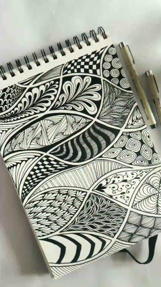 a spiral notebook with black and white doodles on it, next to a pen