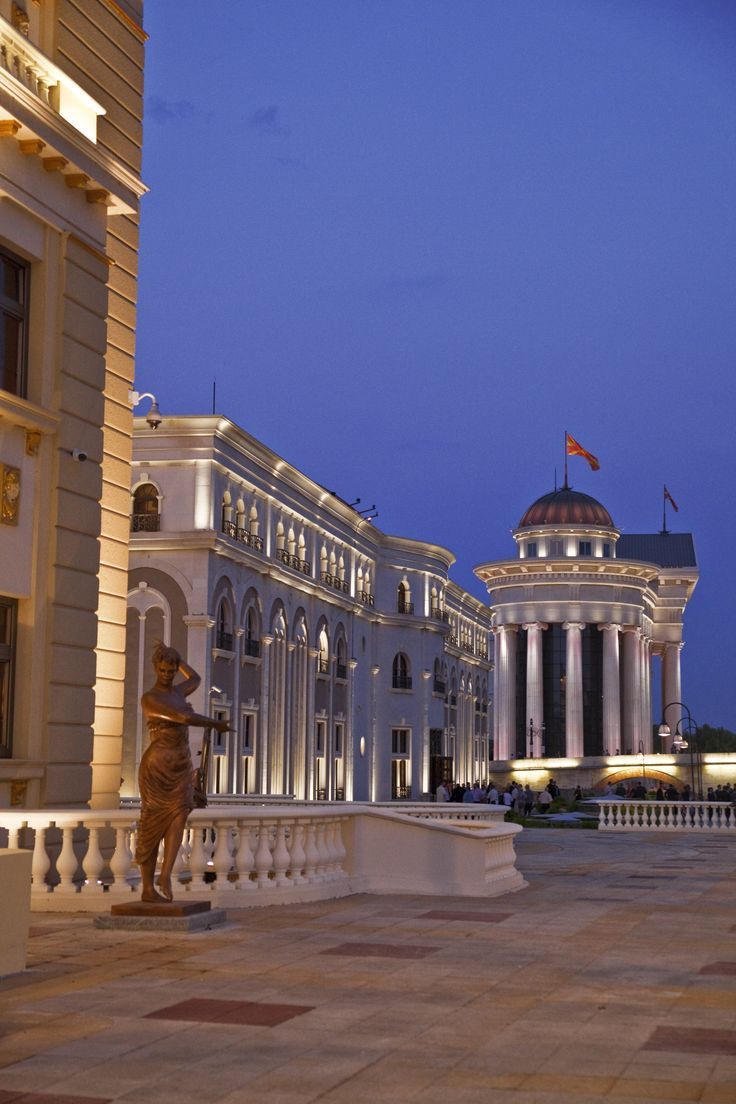 a large building that is lit up in the evening with lights on and statues outside