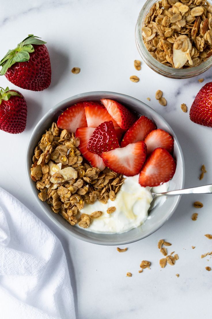 yogurt, granola and strawberries in a bowl on a white table