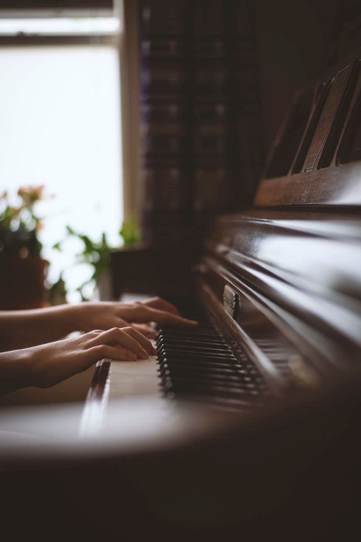 a person is playing the piano with their hand on it's keys and there are plants in the background