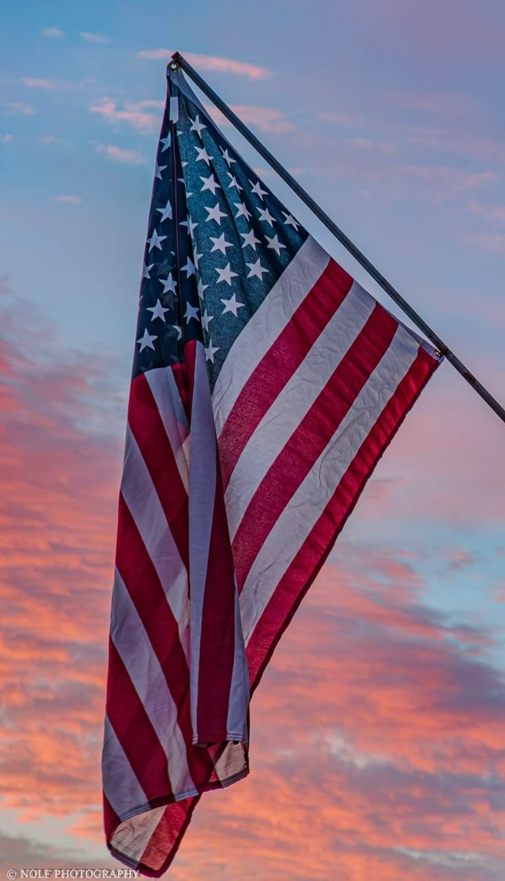 an american flag flying in the sky at sunset