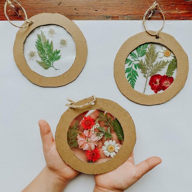 two handmade ornaments are being held in front of a white table with red and green flowers