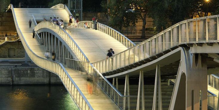 people walking across a bridge over water at night