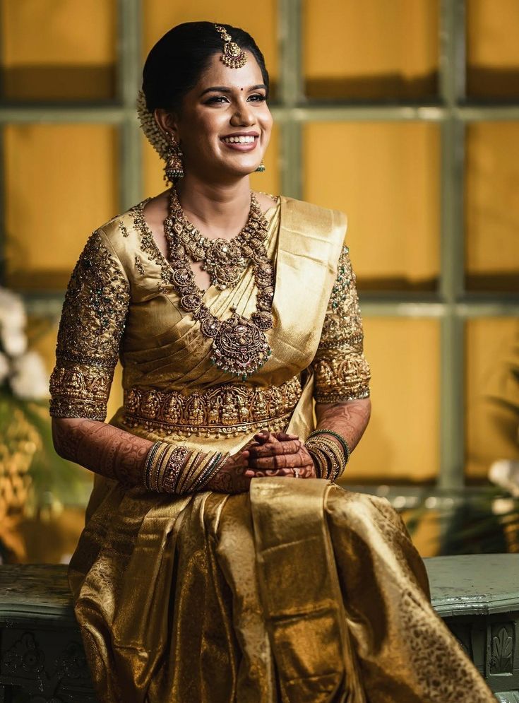 a woman in a gold sari sitting on a bench with her hands clasped to her chest