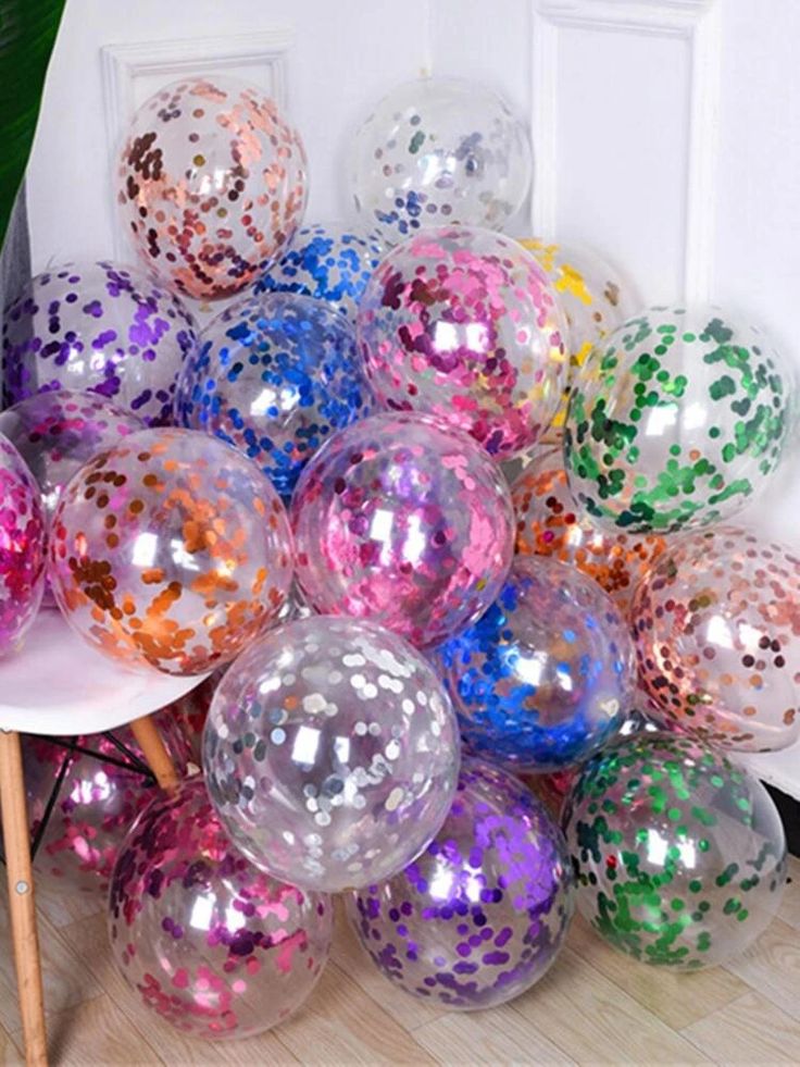 a bunch of shiny balloons sitting on top of a wooden floor next to a potted plant