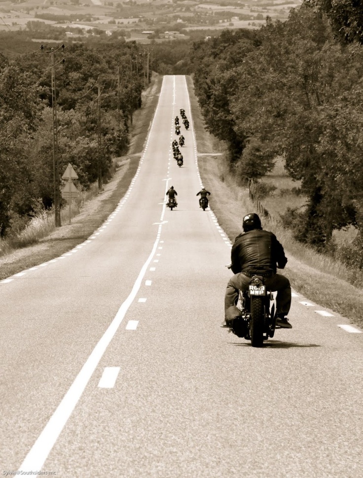 several motorcyclists are riding down the road in black and white photo with trees on both sides