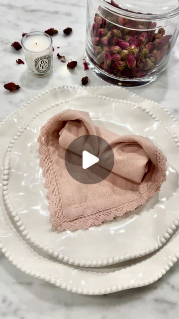 two white plates topped with pink napkins next to a glass container filled with rose petals