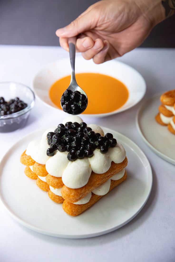 a person is spooning blueberries out of a cake on a plate with orange sauce in the background