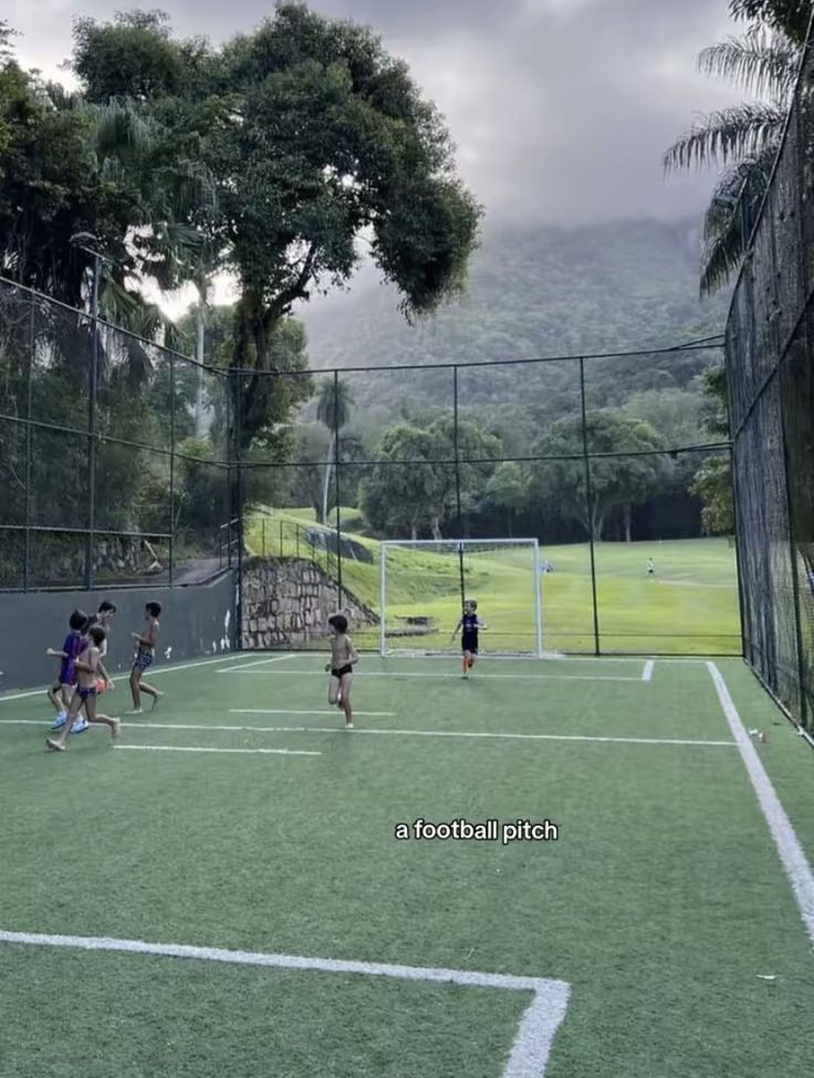 kids playing soccer on a grass field with mountains in the background and trees behind them