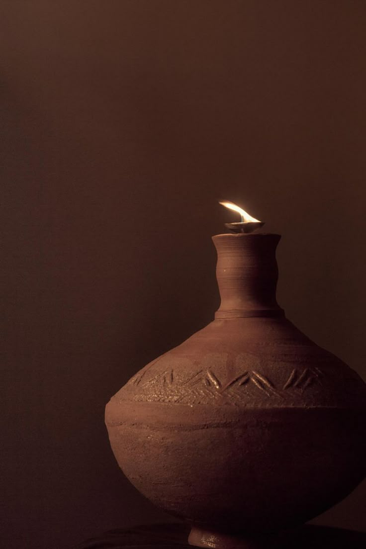 a brown vase with a lit candle in it