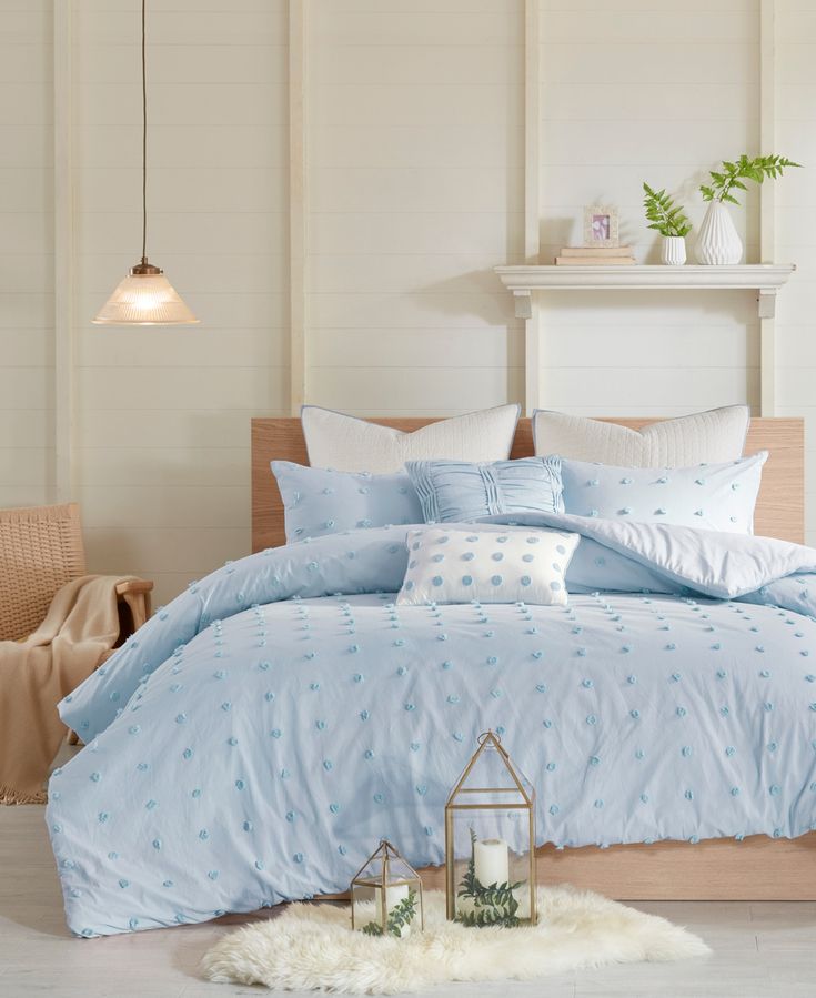 a bed with blue comforter and pillows in a room next to a table, chair and lamp