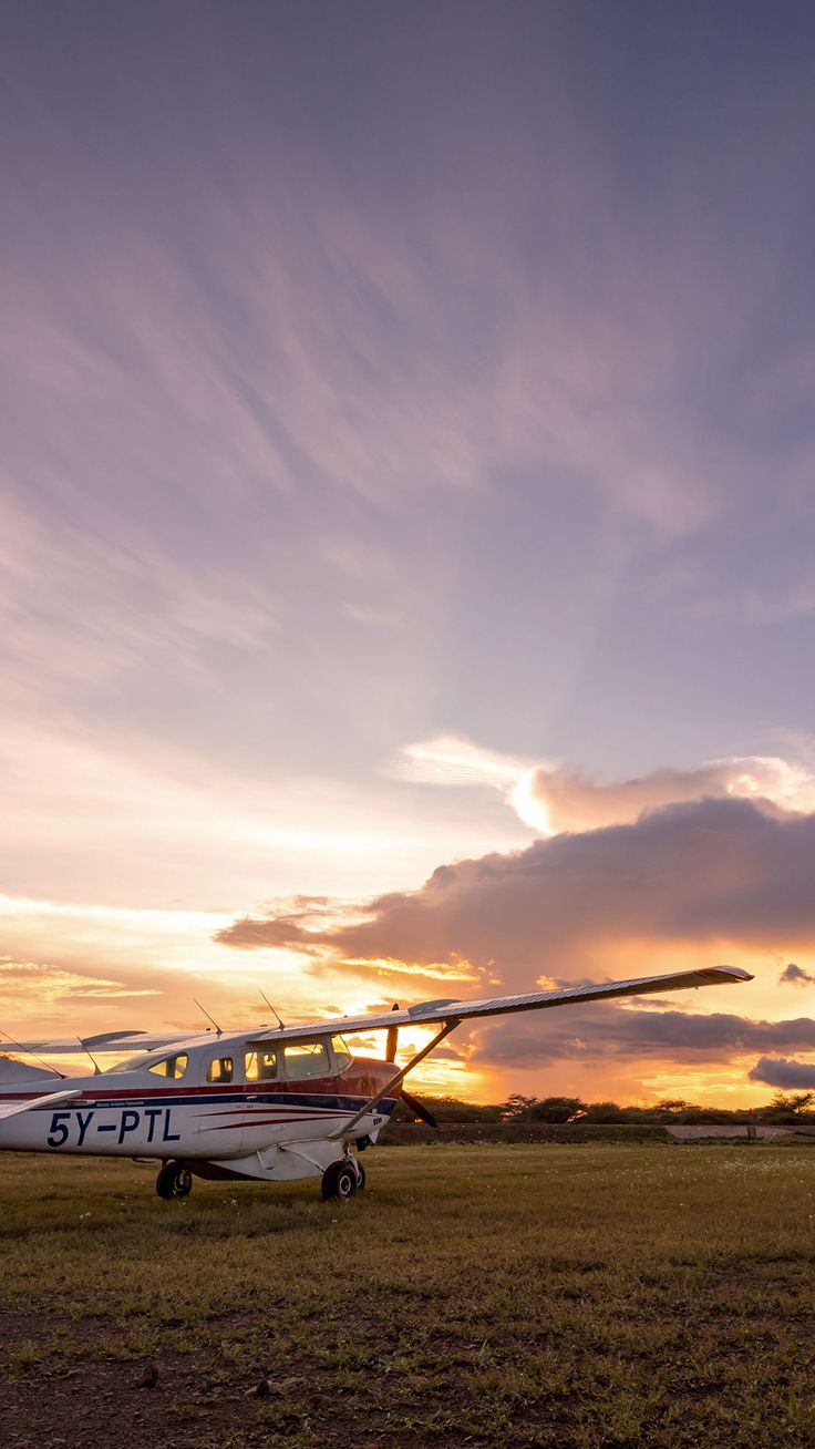 a small airplane sitting on top of an airport tarmac at sunset with clouds in the sky