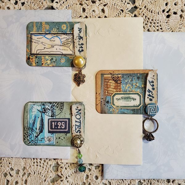 an open book with some charms attached to it on a lace covered table cloth and doily