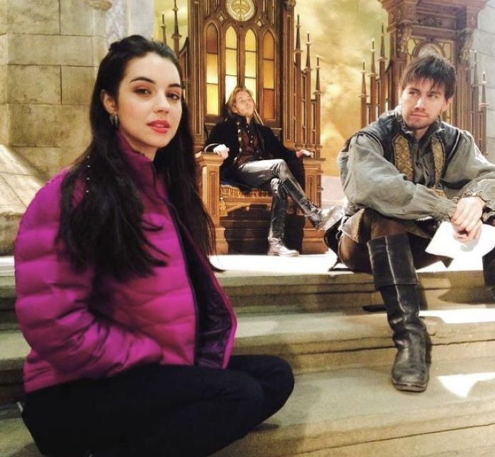 a man and woman sitting on steps in front of a clock tower with other people behind them