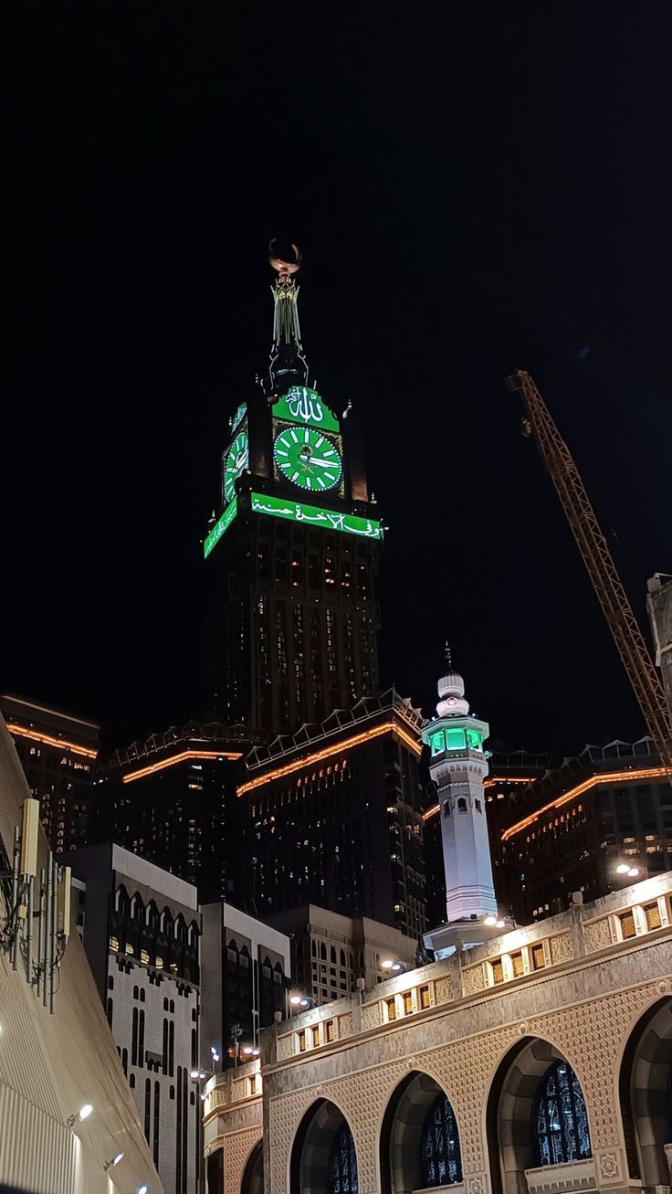 a clock tower lit up in the night sky above other tall buildings and skyscrapers