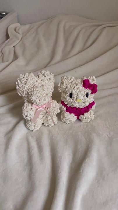 two white teddy bears sitting on top of a bed next to each other with pink bows