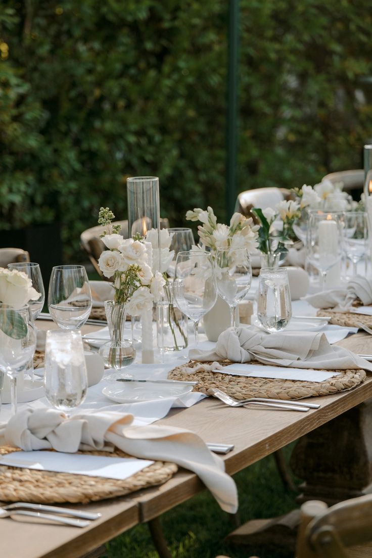 a long table is set with white flowers and place settings for an outdoor dinner party