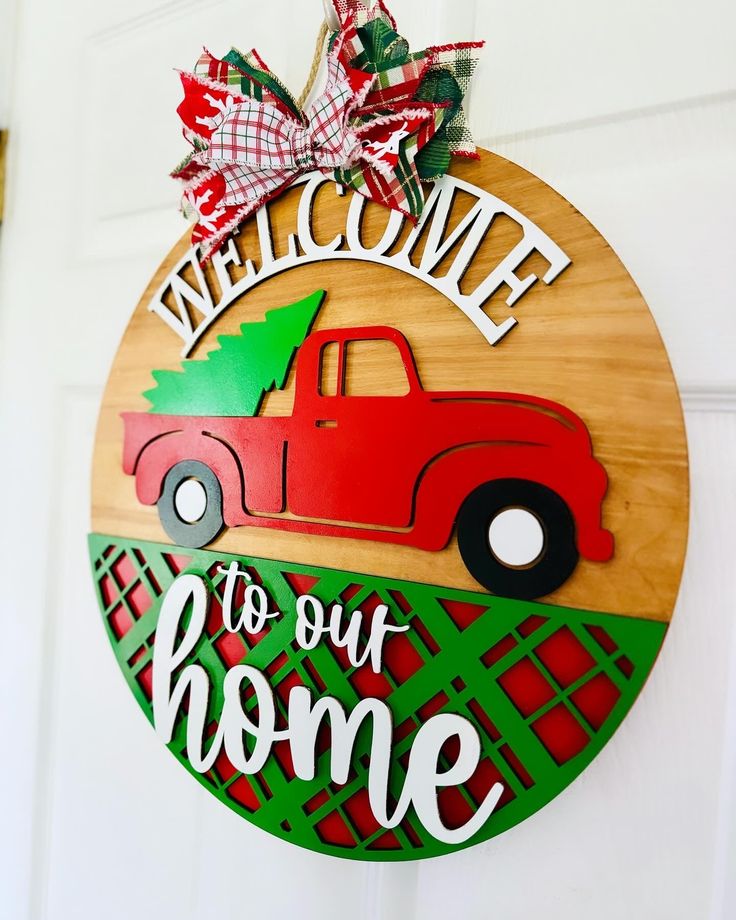 a welcome sign hanging on the front door of a home with a red truck and christmas tree