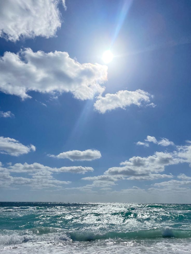 the sun shines brightly over the ocean on a sunny day with blue skies and white clouds