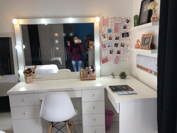 a woman taking a selfie in the mirror at her desk with white chair and lights on