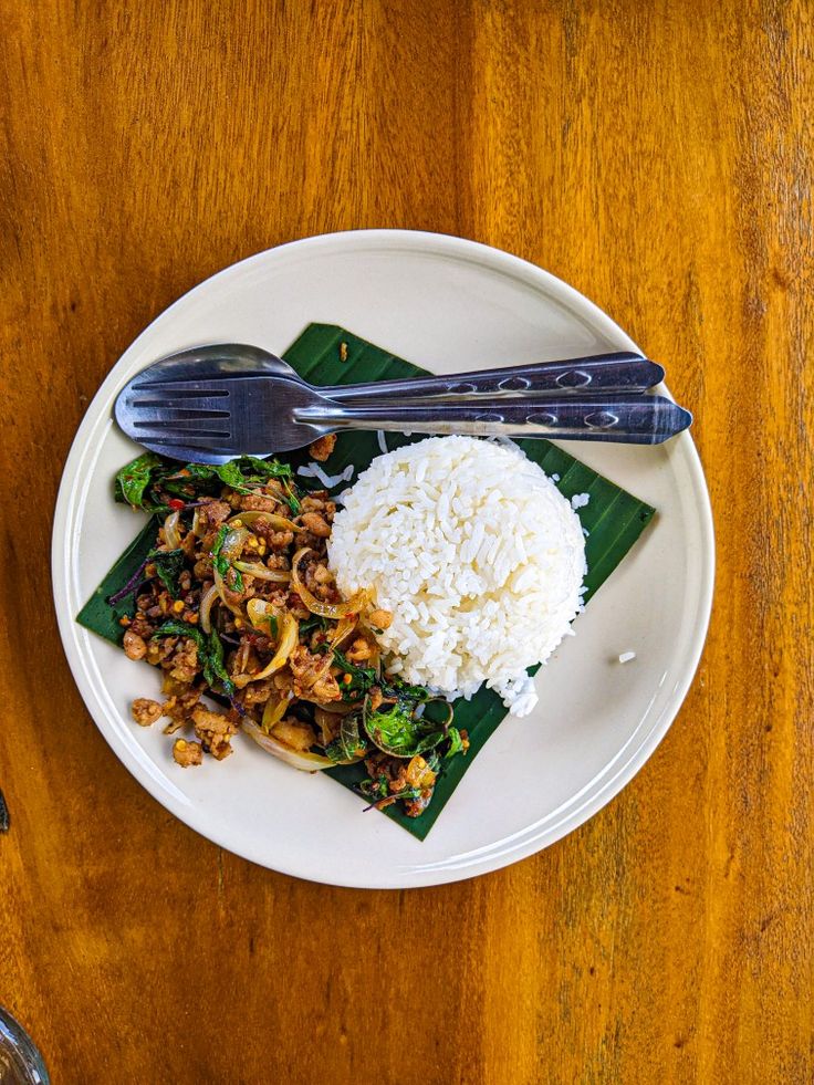 a white plate topped with rice, meat and veggies on top of a wooden table