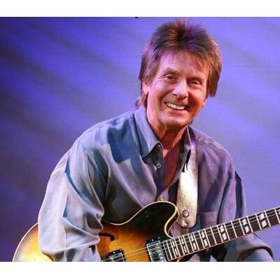 a man smiling while playing an electric guitar