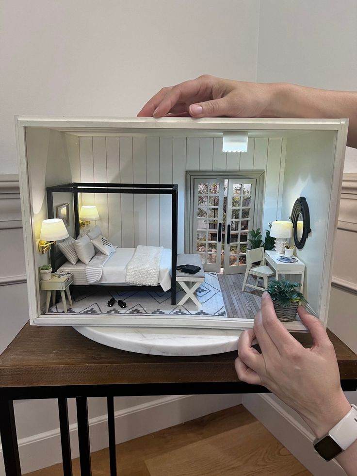 a person holding up a model of a house in the shape of a bed and desk