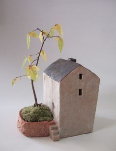 a small house next to a potted plant on a white surface with grey background