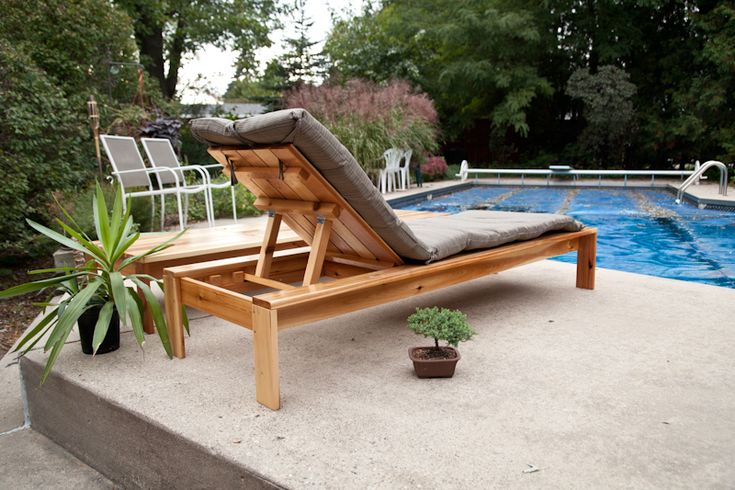 a wooden lounge chair sitting next to a pool in the middle of a backyard area