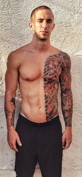 a man with tattoos standing in front of a white wall wearing black shorts and no shirt