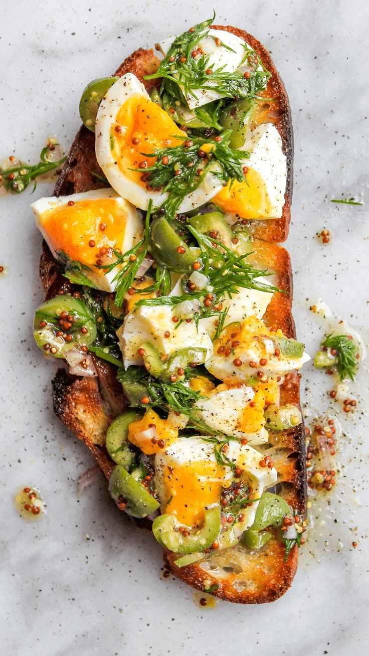 an open face sandwich topped with eggs and vegetables