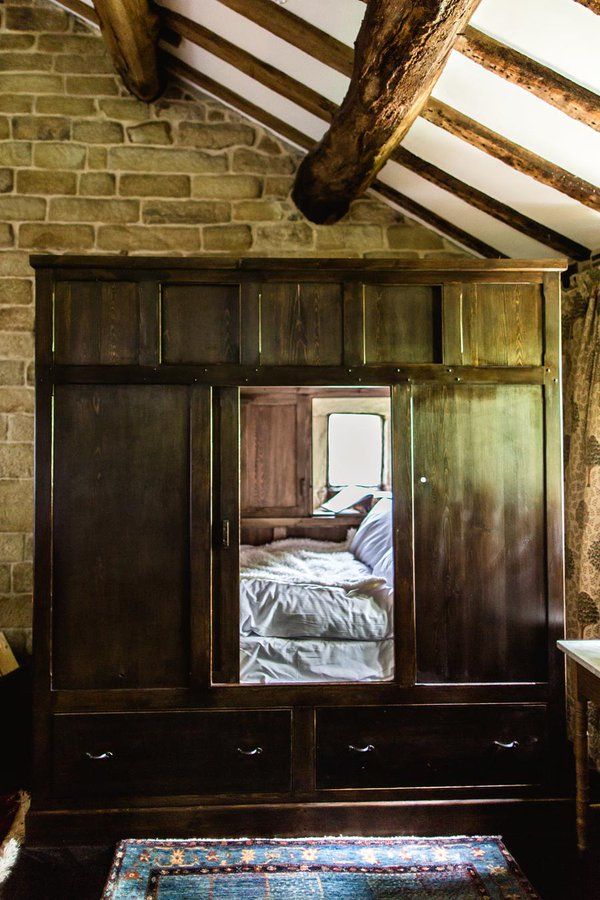 a bedroom with a brick wall and wooden furniture in the corner, looking into an open closet