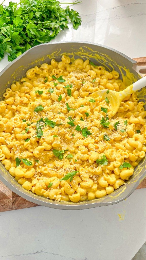 a pot filled with macaroni and cheese on top of a wooden cutting board