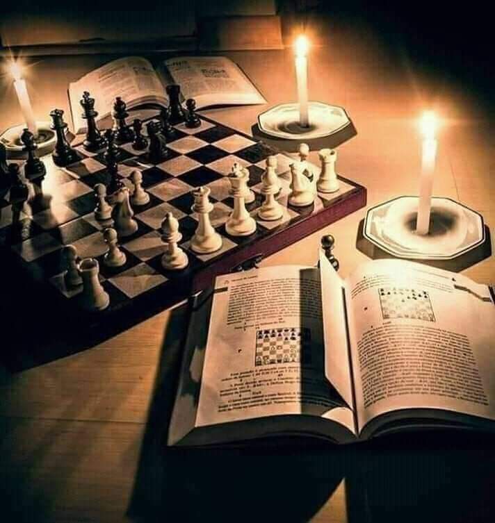 an open book sitting on top of a wooden table next to chess pieces and candles