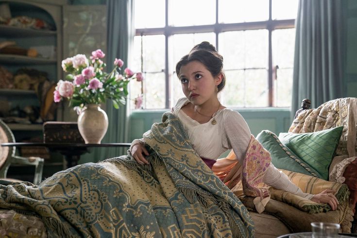 a woman sitting on top of a couch covered in a blanket next to a window