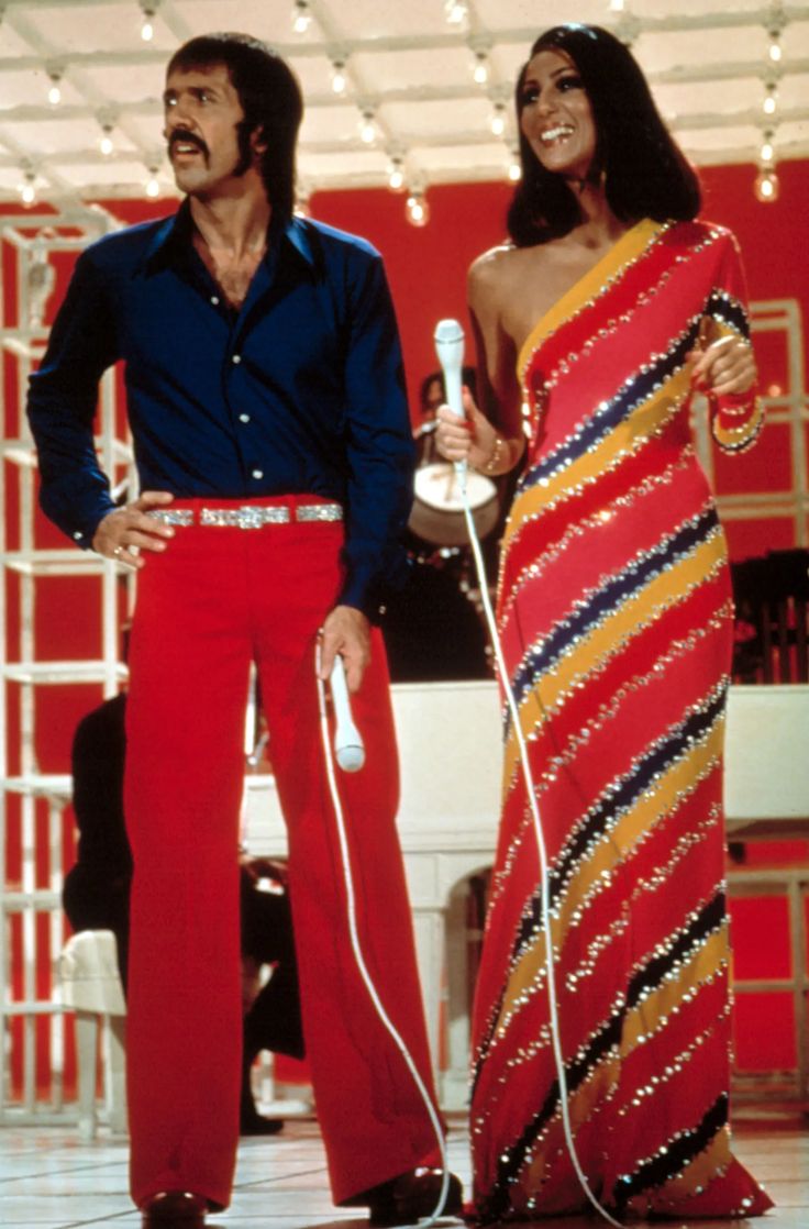 two people standing next to each other with microphones in hand and one person wearing red pants