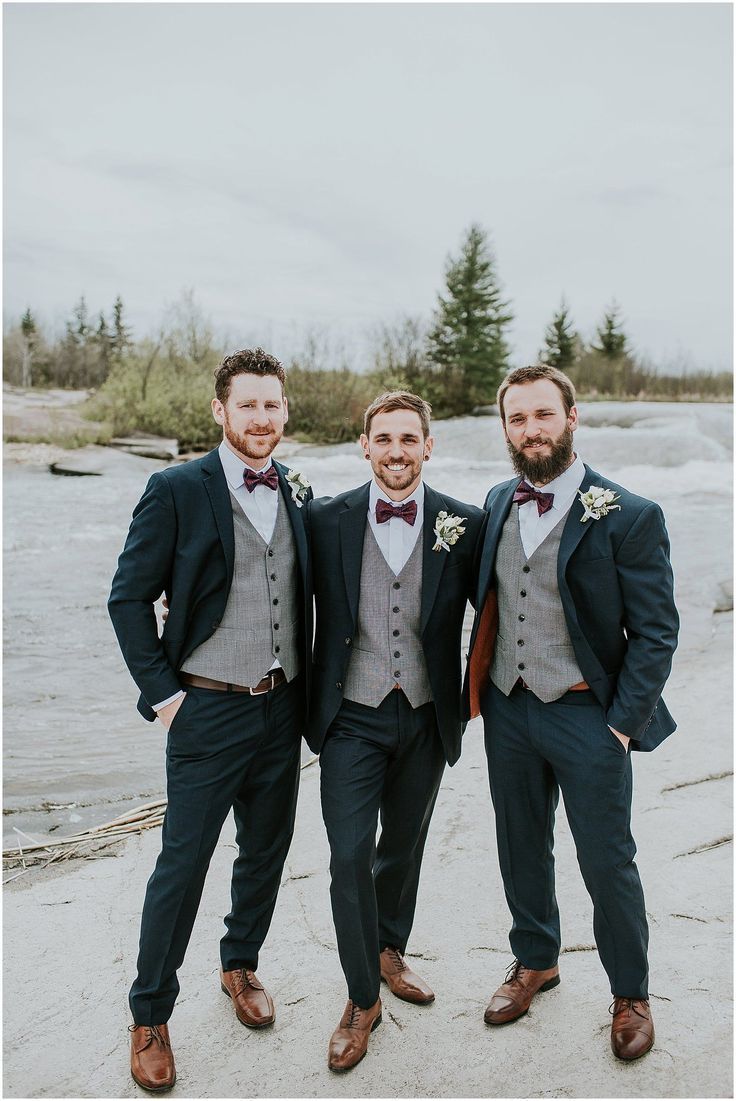 three men in suits and bow ties standing next to each other on the beach with trees in the background