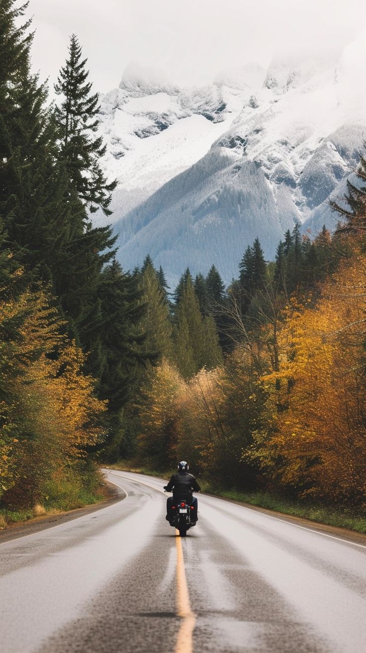 a person riding a motorcycle down the middle of a road with mountains in the background