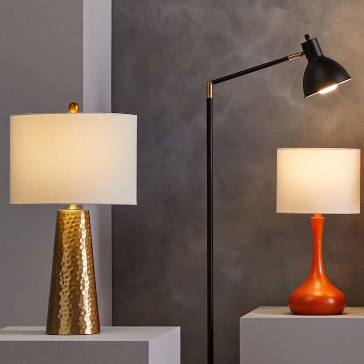 two lamps sitting on top of white pedestals next to each other in front of a gray wall