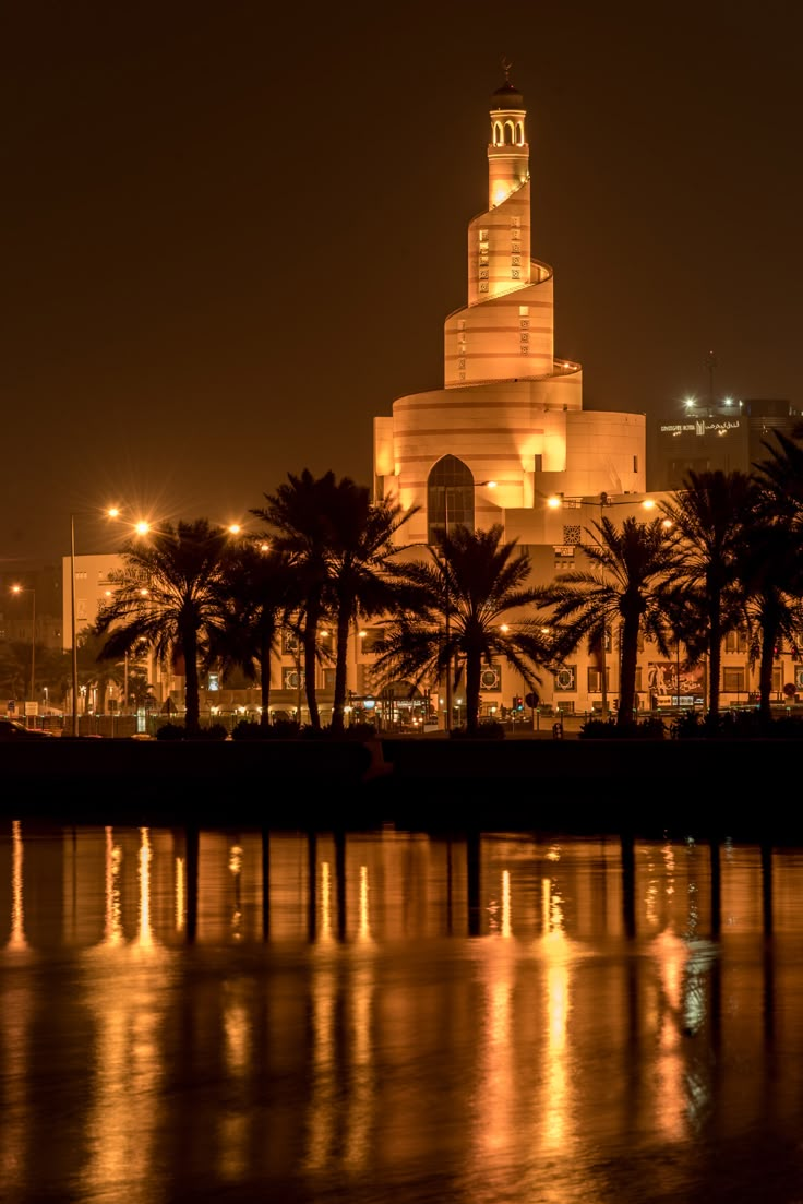 a large building that is lit up in the night with palm trees and lights around it