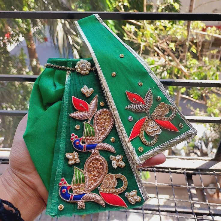 a hand holding a green purse with designs on it