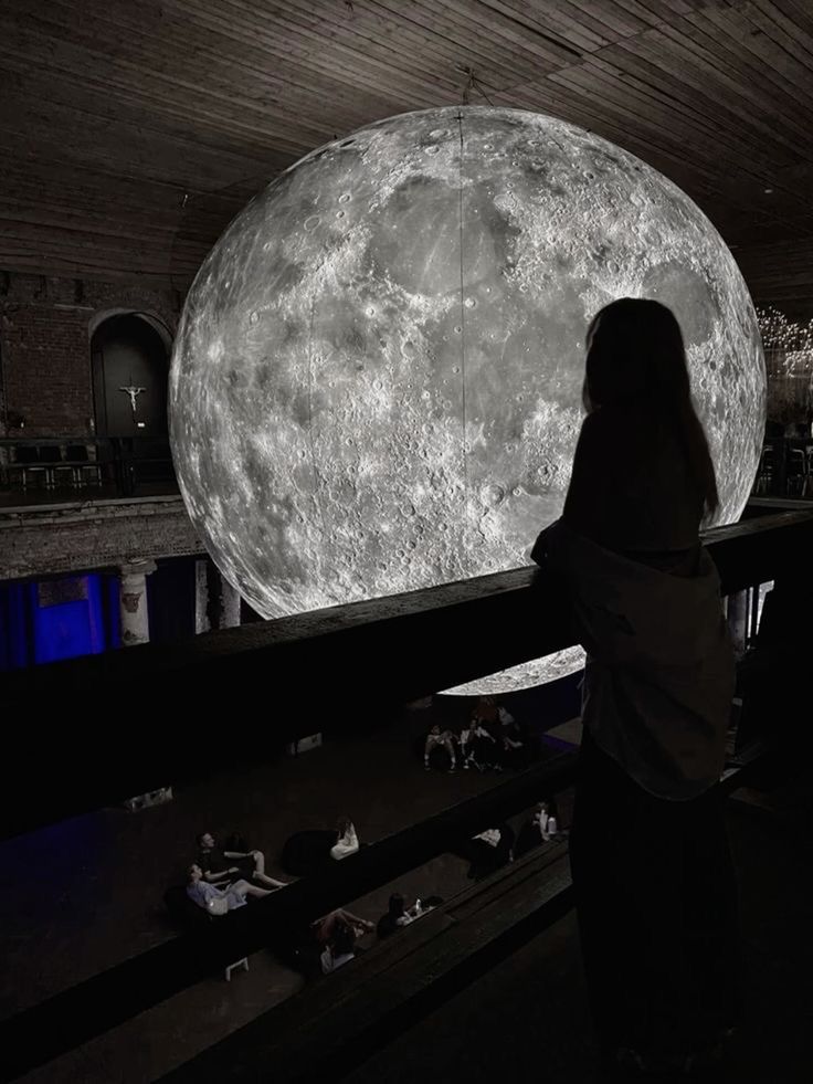 a woman standing in front of a large moon projected on the wall above her head