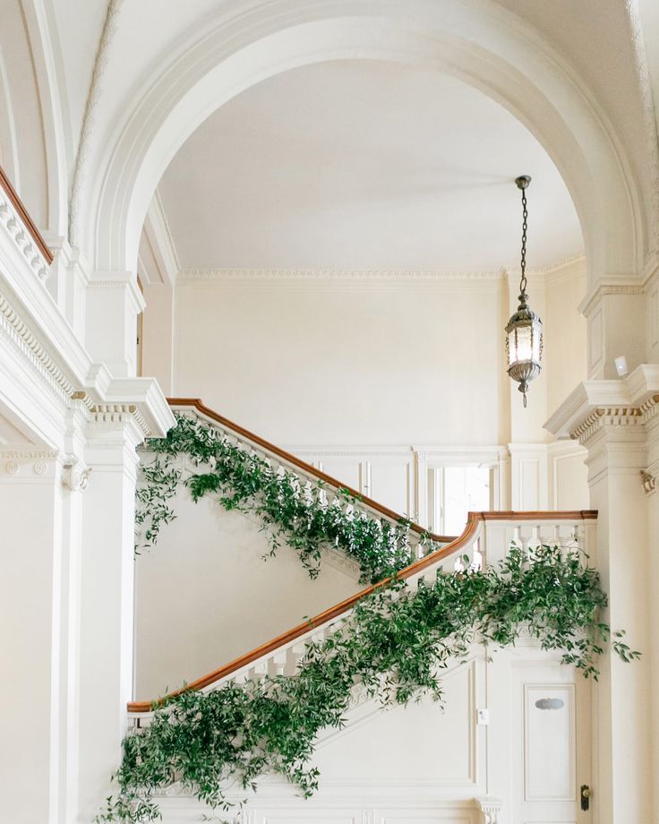 an indoor stair case with plants growing on the railing and in between it is a chandelier