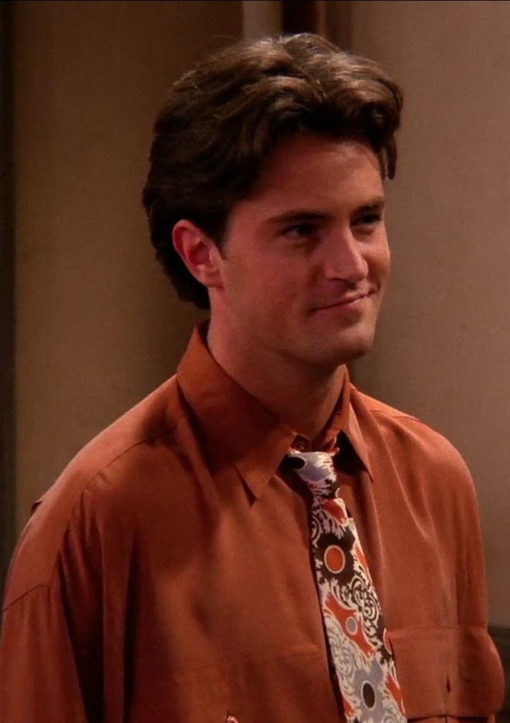 the young man is dressed in an orange shirt and tie with paisley print on it