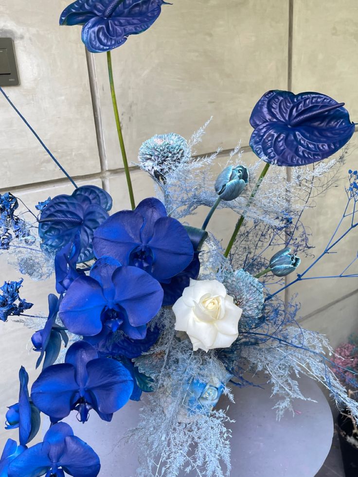 blue and white flowers are arranged in a vase on a round table with silver accents