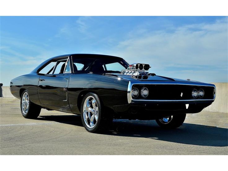 a black muscle car parked on top of a parking lot next to a cement wall