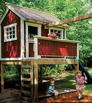 two children playing on a wooden play house in the woods with a slide and swing set