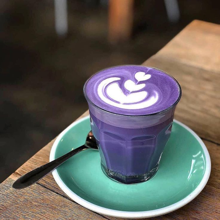 there is a purple drink on top of a green plate with a spoon in it